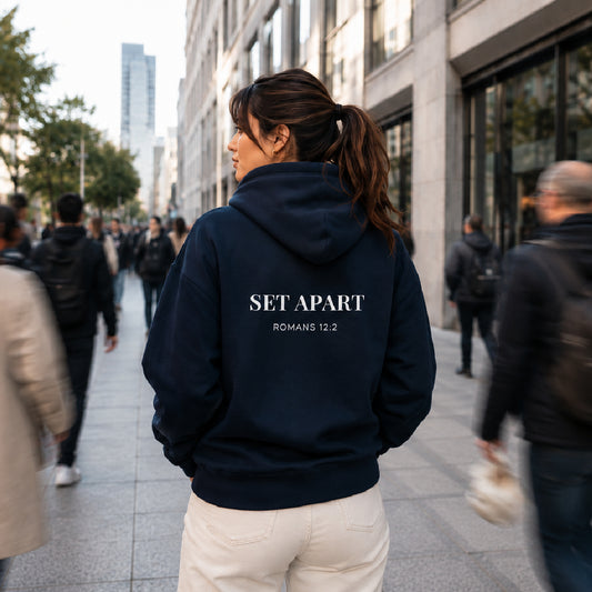 Person wearing a Cornerstone wera navy hoodie with 'Set Apart' text on the back, walking down a city street.