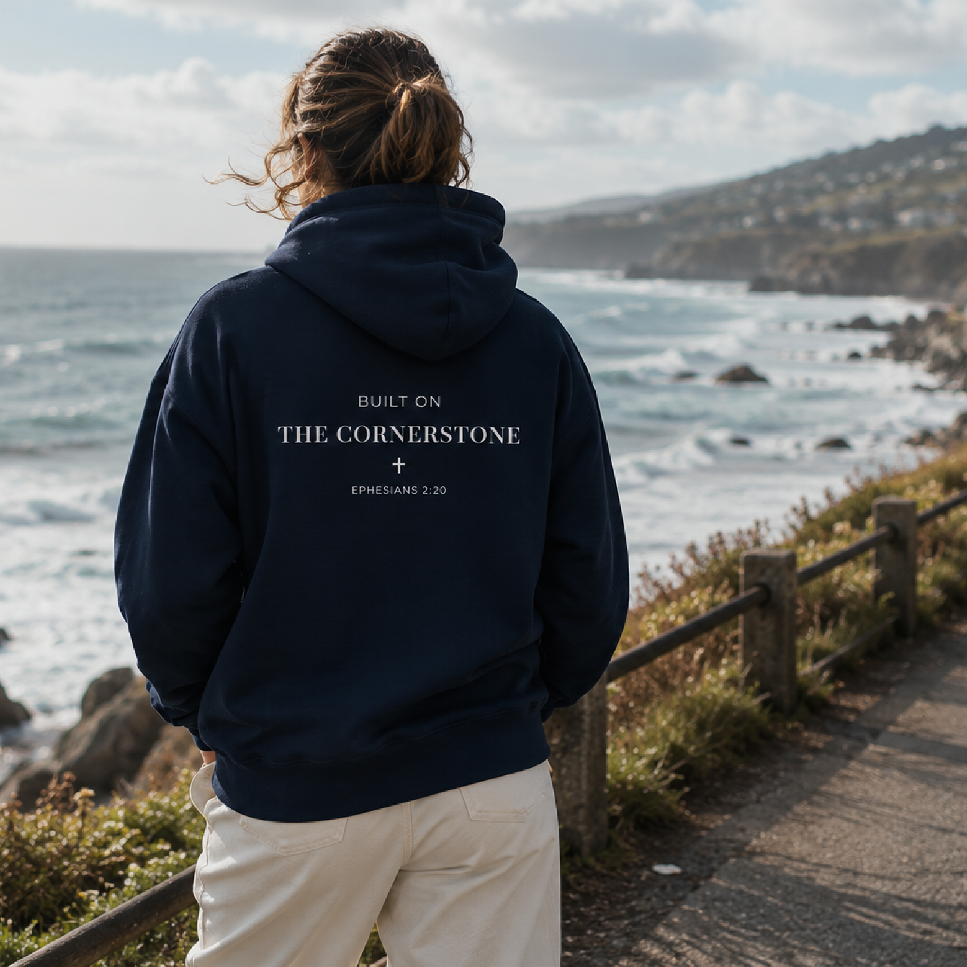 Person wearing a cornerstone wear navy hoodie with text standing on a coastal path