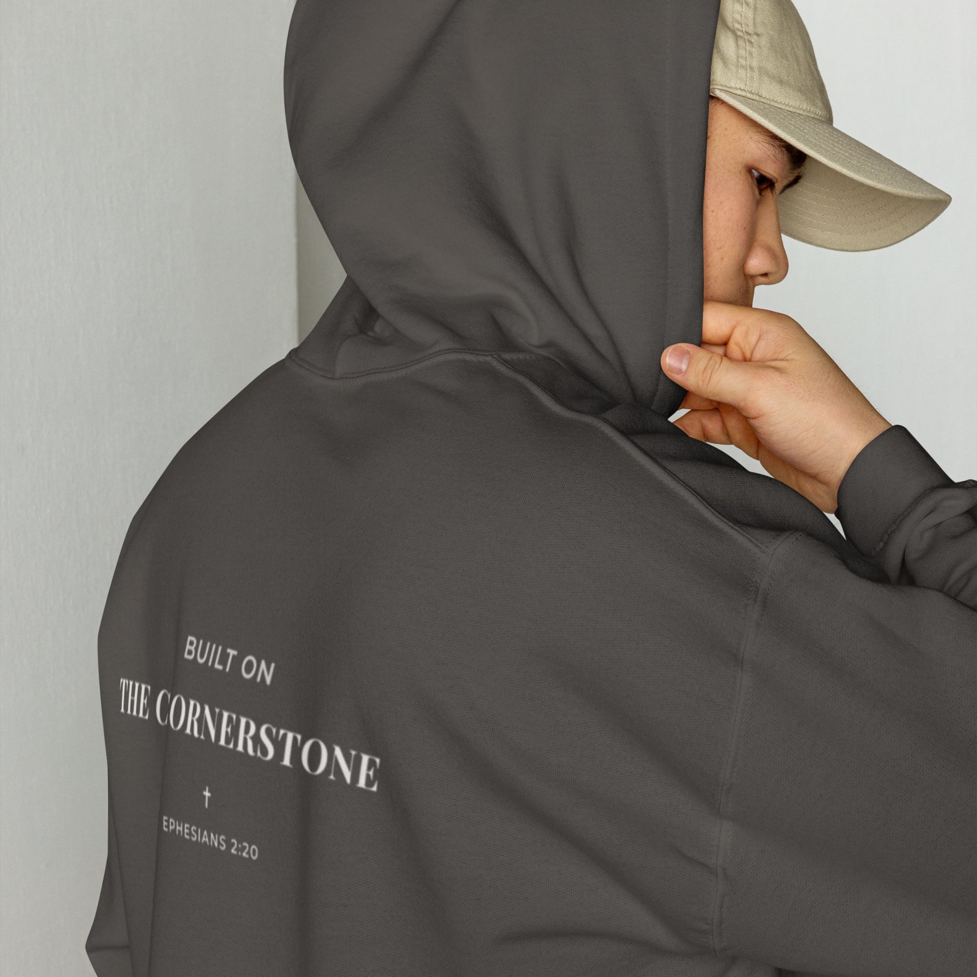 Person wearing a Cornerstone Wear unisex dark grey hoodie with text, standing against a plain background