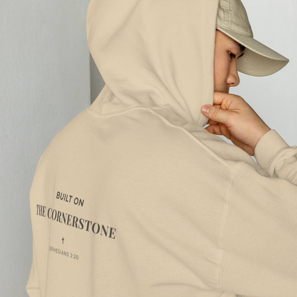 Person wearing a Cornerstone Wear unisex sand hoodie with text, standing against a plain background