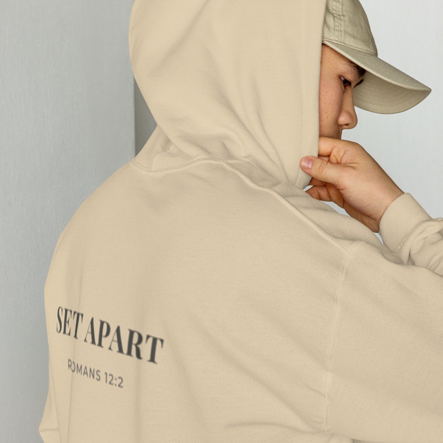 Person wearing a Cornerstone Wear unisex beige hoodie with text, standing against a plain background